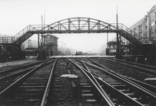 857338 Gezicht op de spoorwegovergang in de Linnaeusstraat te Amsterdam, met de voetbrug en links op de achtergrond het ...